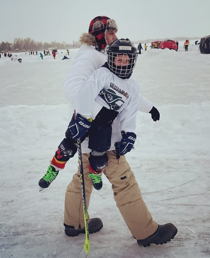 Tyler carrying Levi in full gear across the ice at a pond hockey festival